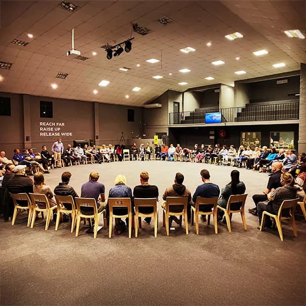 A large group sits in a circle in an auditorium.