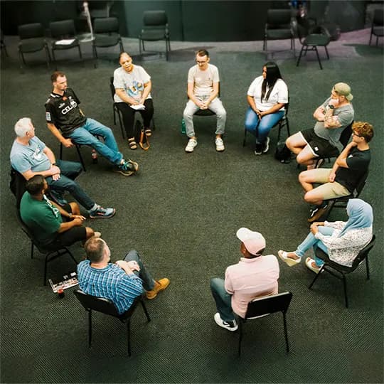 A diverse group of people sitting together in a circle for a recovery meeting.