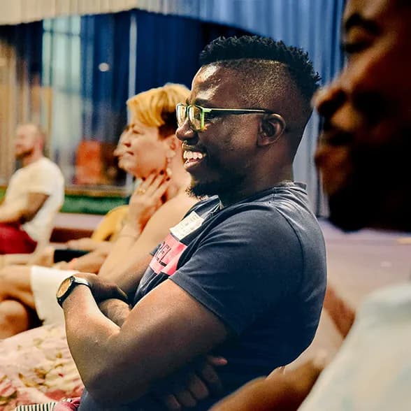 A man with glasses and a mohawk smiles while seated.
