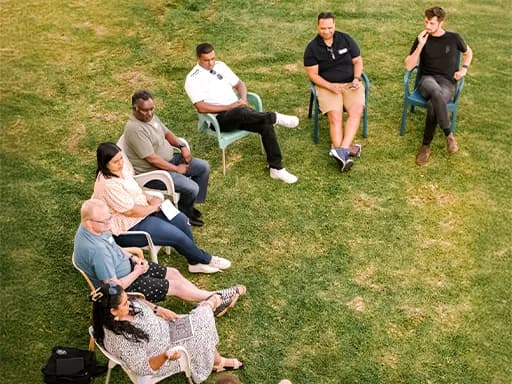 A group of people sits in chairs on the grass.